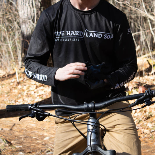 Man in black long sleeve MTB shirt sitting on mountain bike while putting gloves on